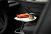 Weißer Getränkehaltertisch für Tesla mit Kaffeebecher und orangefarbener Tasche, neben der Mittelarmlehne befestigt.