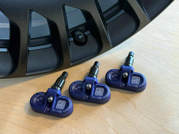4x BLE-TPMS-Reifendrucksensoren für Tesla neben einer schwarzen Autofelge.