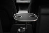Schwarzer Tesla Model 3 Tisch mit zwei Getränkehaltern und silberfarbenem Rand, von der Rückbank zwischen den Vordersitzen gesehen.