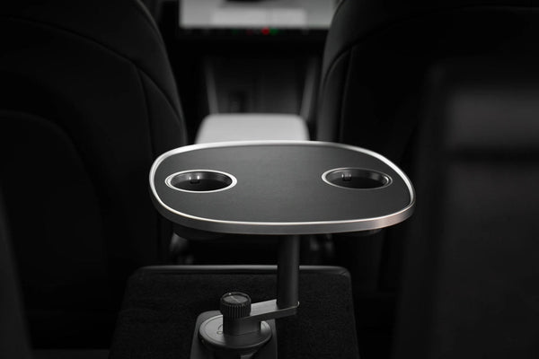 Schwarzer Tesla Model 3 Tisch mit zwei Getränkehaltern und silberfarbenem Rand, von der Rückbank zwischen den Vordersitzen gesehen.