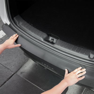 Zwei Hände platzieren den Spigen Ladekantenschutz für Tesla Model Y auf der hinteren Stoßstange unter dem offenen Kofferraum.