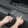 Hände ziehen die transparente Folie vom Spigen Ladekantenschutz für Tesla Model Y an der Ladekante ab.