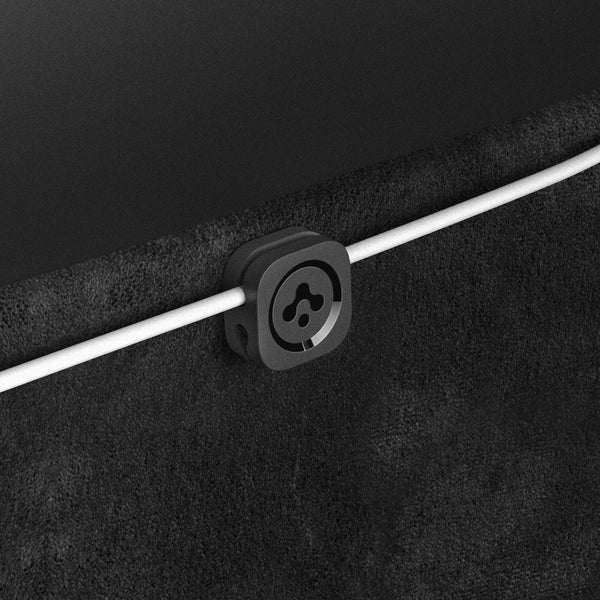 Detail eines schwarzen Kabelclips mit Spigen-Logo, der ein weißes Kabel der Tesla-Ladestation an der dunklen Verkleidung hält.