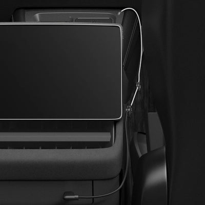 Tesla-Ladestation teilweise hinter einem großen schwarzen Bildschirm, mit weißem Kabel und schwarzem Anschlusskabel entlang der Mittelkonsole.