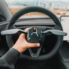 Installation der s3xy Tesla Stalk Tesla Model 3 Highland, gehalten vor dem Lenkrad, zeigt Blinkerhebel Nachruestung mit originalgetreuem Look