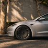 Silbernes Tesla Model 3 Highland am Straßenrand, Nahaufnahme der CHELA-Vorderfelge in Glossy Titanium mit Satin Carbon.