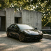 Schwarzes Tesla Model 3 mit The New Aero CHELA in Matte Bronze und Satin Carbon vor moderner Betonarchitektur.