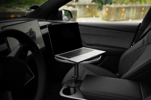 Car Table Tesla Model 3 mit aufgeklapptem Laptop über der Mittelkonsole, neben dem Lenkrad und dem schwarzen Beifahrersitz.