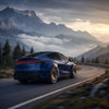 Blaues Tesla Model Y Juniper mit CHELA Felgen in Glossy Titanium und Satin Carbon bei der Fahrt durch eine Berglandschaft.