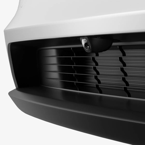 Tesla Model Y Juniper Zubehör: Spigen Frontkamera-Schutzglas unter der weißen Frontstoßstange, über dem schwarzen Kühlergrill.