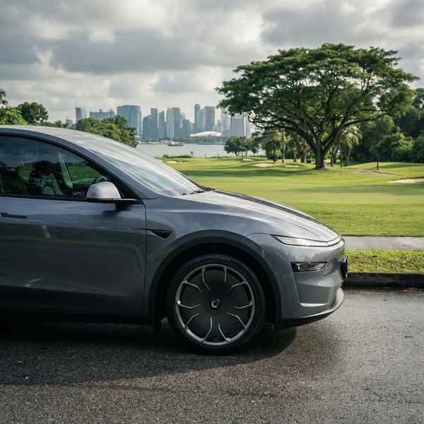 Graues Tesla Model Y Juniper mit CHELA 20-Zoll-Felgen in Glossy Titanium und Satin Carbon, Nahaufnahme im grünen Stadtumfeld.