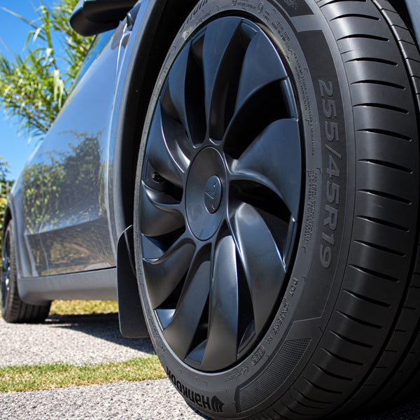 Tesla Model Y Juniper Radkappen 19 Zoll Uberturbine aus niedriger Perspektive, mit Reifenprofil und grauem Fahrzeug im Hintergrund