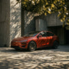 Rotes Tesla Model Y Juniper mit CHELA Felgen in Glossy Titanium und Satin Carbon vor moderner Architektur.