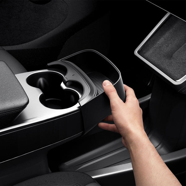 Eine Hand hält die schwarze Tesla Model Y Mittelkonsolen-Erweiterung an die Mittelkonsole neben den beiden Getränkehaltern.