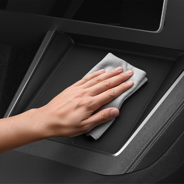 Eine Hand wischt mit einem grauen Tuch über die schwarze Tesla Model Y Schutzauflage in der Mittelkonsole.