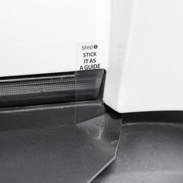 Detail des Tesla Stoßstangenschutzes an einer weißen Karosserie, mit transparenter Ausrichtlasche neben einer Leuchte.