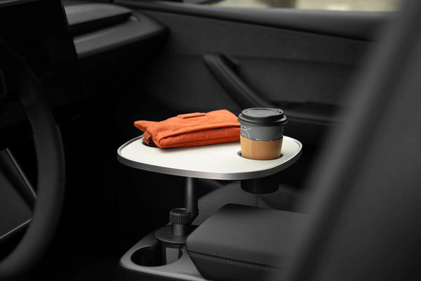 Weißer Tesla Model 3 Tisch in der Mittelkonsole mit einem Kaffeebecher und einer orangefarbenen Tasche auf der Platte.